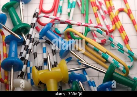 Verschiedene Büroklammern und Druckstifte sind zufällig auf Graphpapier angeordnet. Stockfoto