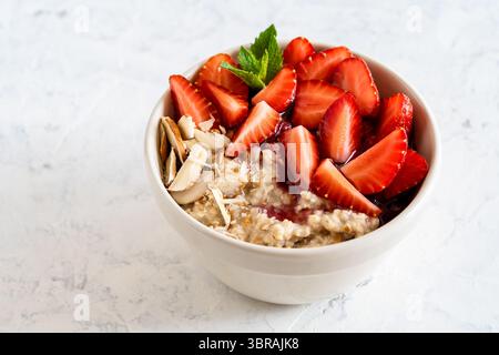 Mehrkörnige Haferbrei-Schüssel mit frischen Erdbeeren, Beerenmarmelade und Nüssen. Gesunder Frühstücksbrei Stockfoto