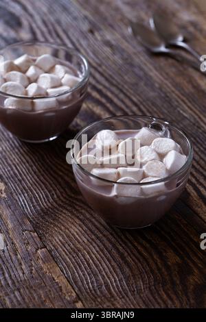 Süße heiße Schokolade mit Marshmallows in Glasbecher auf hölzernem Hintergrund Stockfoto