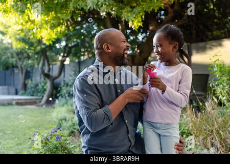 Afroamerikanischer Vater und Tochter spielen mit Blasenflasche und Zauberstab und machen Blasen im Hinterhof Stockfoto