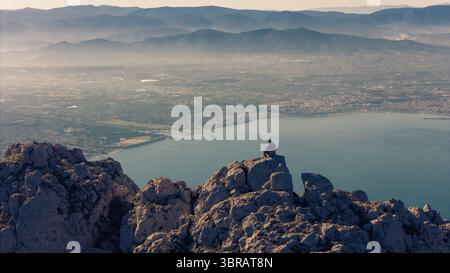 Aus der Vogelperspektive einer Einzelfigur auf zerklüfteten Gipfeln mit Blick auf die ruhige Küste, Olympos, Katerini, Griechenland. Stockfoto