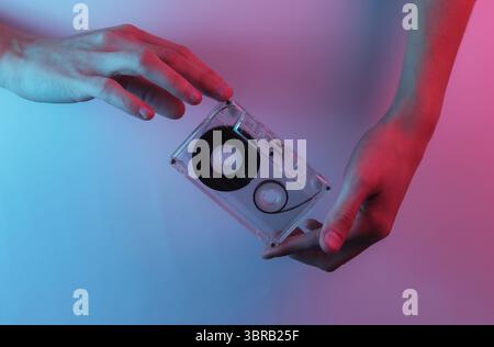 Retro Wave 80s Hände halten die Audiokassette. Kreative Pop-Art-Neonfarben in Pink Blau. Trendige Farbverlaufsbeleuchtung. Nachtlicht Stockfoto