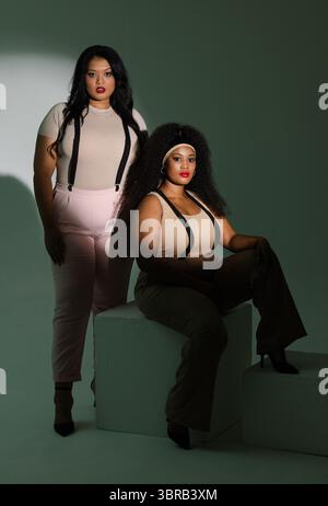 Verschiedene weibliche Models posieren im Studio in neutralen Oberteilen mit Hosenträgern auf weißen Würfeln unter Lichtern Stockfoto