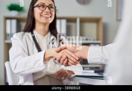 Lächelnde Ärztin schüttelt die Hände mit dem Patienten in der Arztpraxis, zeigt Unterstützung und Pflege. Stockfoto
