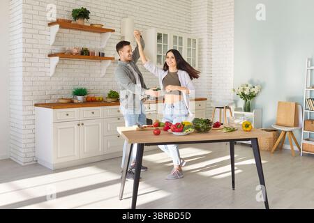 Verliebte Paare tanzen zusammen in der Küche, bereiten Essen für ein romantisches Abendessen vor, verbringen Zeit miteinander Stockfoto