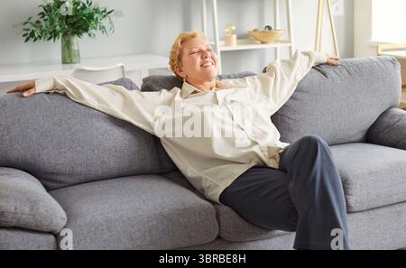 Ältere, entspannte ältere Frau im Ruhestand angenehme Frau, die sich auf einer neuen grauen weichen Couch in einem stilvollen, gemütlichen Apartment ausruht Stockfoto