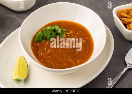 Scharfe mexikanische Hühnersuppe mit Nudeln, garniert mit frischem Koriander und Limettenkeil Stockfoto