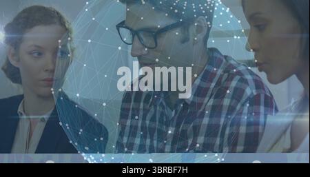 Bürotrio, das sich über den Schreibtisch im Konferenzraum beugt, mit durchscheinender Netzwerkkugel Stockfoto