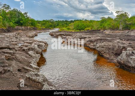 Ein ruhiger Fluss fließt durch felsiges Gelände, umgeben von üppiger Vegetation, und zeigt die natürliche Schönheit von Guaviare, Kolumbien. Stockfoto