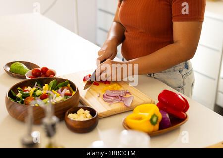 Asiatische Frau schneidet rote Paprika auf Schneidebrett an der Küchentheke mit einem Kochmesser Stockfoto