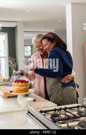 Diverse Seniorenpaare stehen in der Küche und dekorieren mehrschichtigen Biskuitkuchen mit Beeren Stockfoto