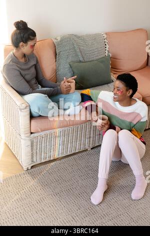 Verschiedene Freundinnen unterhalten sich im Wohnzimmer, tragen Gelaugenflicken und schlürfen Keramikbecher Stockfoto
