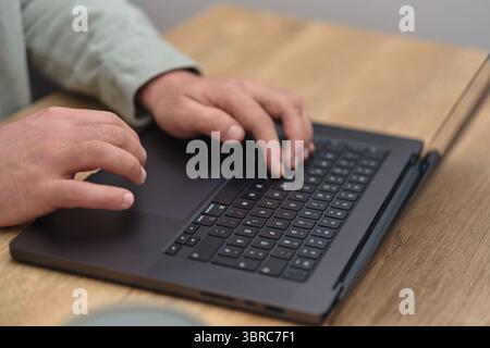 Nahaufnahme eines Geschäftsmannes, der auf der Laptop-Tastatur auf dem Holztisch arbeitet und tippt. Stockfoto