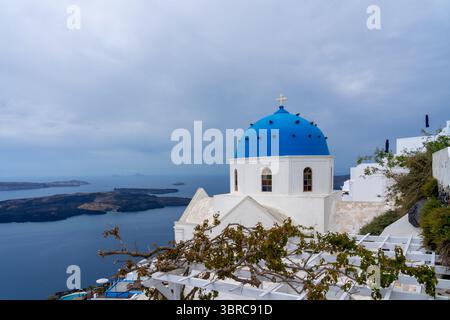 Kirche der Auferstehung des Herrn mit Weinrebe auf Spalier im Vordergrund in Fira, Santorin, Griechenland. Stockfoto