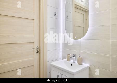 Das ist ein modernes Badezimmer mit stilvollem Waschbecken und beleuchtetem Spiegel für ein Ambiente Stockfoto