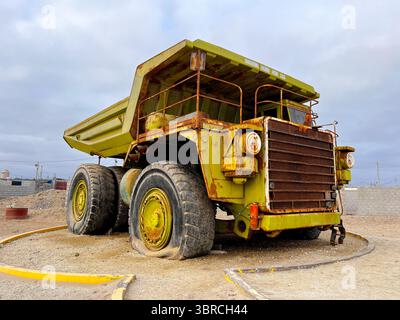 Großer alter Müllwagen. Großer grüner, rostiger Bergbauwagen außer Betrieb, der an der Küste Perus in San Juan de Marcona ausgestellt wird. Stockfoto