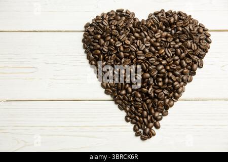 Mit herzförmigem, dunklem Kaffeebohnenstapel auf lackierter weißer Holzplatte in flachem Design Stockfoto