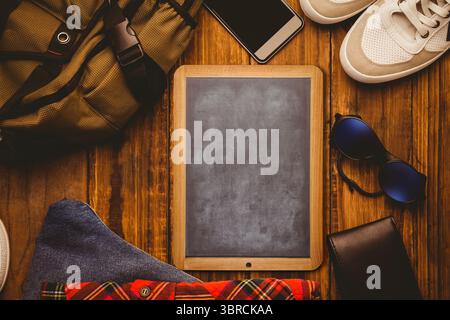 Die Tablette mit Kreidetafel ist flach auf Holzoberfläche mit Rucksack, Telefon und Turnschuhen zu sehen Stockfoto