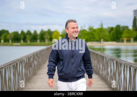 Aktiver Seniorenmann, der auf einer Holzbrücke in einem Park läuft. Stockfoto