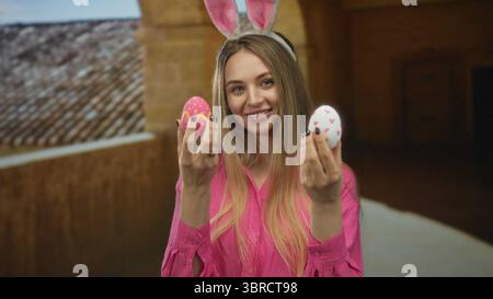 Eine junge Frau mit Hasenohren hält farbenfrohe ostereier in einem historischen Universitätsgebäude, in dem eine fröhliche, festliche Atmosphäre drinnen herrscht. Stockfoto