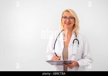 Selbstbewusste Therapeutin, blond, mit weißem Labormantel und Stethoskop, auf weißem Hintergrund mit leerem Platz für Text. Gesundheitswesen und medizinisches Berufskonzept. Stockfoto