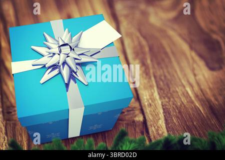 Flache blaue Geschenkbox mit weißem Band, silberner Schleife auf dem Tisch mit Kiefernzweig Stockfoto