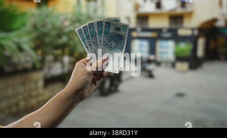 Ein Mann hält polnische Zloty-Banknoten in der Hand auf einer Stadtstraße und zeigt Geld in einer urbanen Umgebung mit verschwommenem Hintergrund. Stockfoto