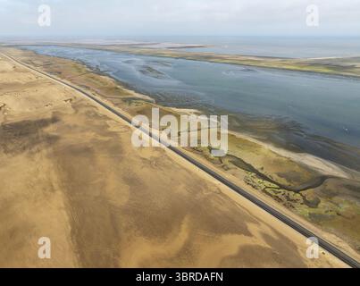 Aus der Vogelperspektive führt eine gerade Straße durch die trockene Landschaft entlang des Brackwassers, der zum Meer führt, Windhoek, Region Khomas, Namibia. Stockfoto