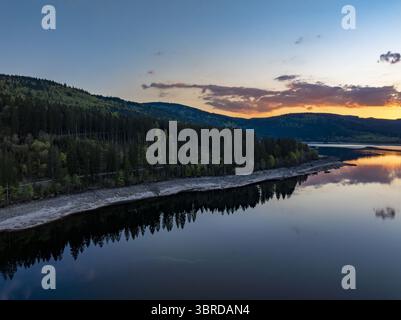 Aus der Vogelperspektive auf den ruhigen See, der den feurigen Sonnenuntergang und den dunklen Wald widerspiegelt und eine ruhige Landschaft entlang des Ufers schafft, Schluchsee, Baden-Württemberg, Deutschland. Stockfoto