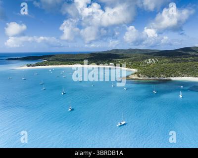 Aus der Vogelperspektive auf türkisfarbenes Wasser umgibt den unberührten weißen Sand von Whitehaven Beach, gesäumt von Segelbooten unter einem Himmel von flauschigen Wolken, Queensland, Australien. Stockfoto