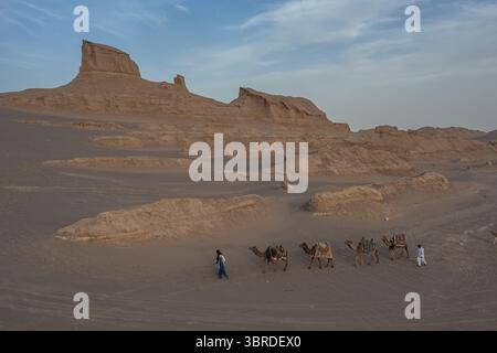 Aus der Vogelperspektive der Wüstenlandschaft, wo der sich verschiebende Sand auf die zerklüfteten Kaluts-Formationen trifft und eine Karawane das trockene Gelände in Kerman, Provinz Kerman, Iran durchquert. Stockfoto