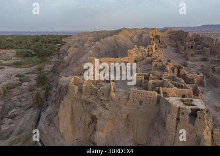 Die raue, sonnendurchflutete Felsklippe, die sich in einem scharfen Kontrast zur grünen Oase im Tal in Kerman, Provinz Kerman, Iran, erhebt sich aus der Vogelperspektive. Stockfoto