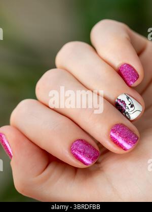 Weibliche Hand mit rosa Maniküre. Frauen-Fingernägel mit rosa holographischem nagellacklack auf grünem üppigem Hintergrund. Das ästhetische Erscheinungsbild des rotvioletten M Stockfoto