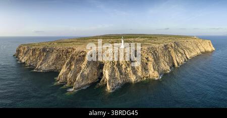 Aus der Vogelperspektive auf eine zerklüftete, sonnenverwöhnte Insel mit steilen Klippen, die ins azurblaue Meer stürzen, gekrönt von einem einsamen Leuchtturm, Bunyola, Balearen, Spanien. Stockfoto