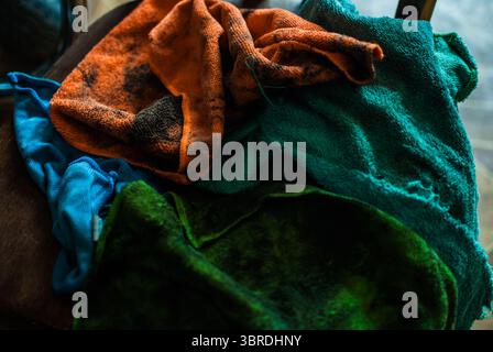 Ein Haufen bunter, schmutziger Lappen, die in der Nähe des Zerkleinerers auf dem Holzstuhl liegen. Alte Garage Stockfoto