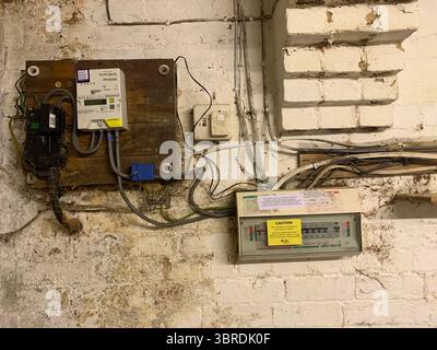 Alte elektrische Verkabelung Haupteinheit Gasbox Rohre Drähte Kabel schmutzig schmuddelig an der Wand in einem Keller Meter Gas Elektrizität Holzrahmen Elektrik UK Stockfoto