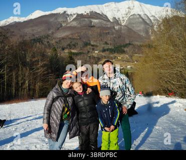 Eine fröhliche Familie mit drei Kindern genießt einen sonnigen Wintertag in einer verschneiten Berglandschaft. Lächelnd und umgänglich schaffen sie wertvolle Erinnerungen Stockfoto
