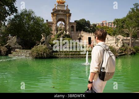 Touristen, die ein Foto von einem Brunnen im Ciutadella Park in Barcelona machen. Typ mit Telefon, Blick von hinten Stockfoto