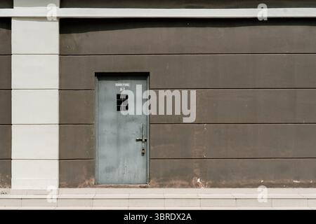 Minimalistisches architektonisches Detail einer Industrietür für einen Panelraum („RUANG PANEL A-1“) an einer braun-weißen Paneelwand mit Stufen unten. Stockfoto