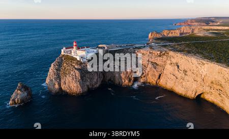 Blick aus der Vogelperspektive auf den schroffen, sonnendurchfluteten Klippen, wo das tiefblaue Meer gegen die Felsen stürzt, Sagres, Faro, Portugal. Stockfoto