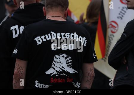 Apolda, Deutschland. Juli 2025. "Bruderschaft C-60" steht auf einem T-Shirt, das von einem Teilnehmer an einer Demonstration auf dem Marktplatz getragen wird. Die jungen Nationalisten Thüringens, die Jugendorganisation der rechtsextremen Partei die Heimat, gehörten zu denen, die die Demonstration forderten. Als Grund für die Demonstration wird ein Messerangriff auf einen Mitarbeiter der Bezirksverwaltung Mitte Juni genannt. Ein Mann aus der Türkei wurde als Verdächtiger verhaftet. Quelle: Bodo Schackow/dpa/Alamy Live News Stockfoto