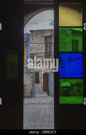 Blick auf ein Steingebäude mit Holztüren und blauen Fensterläden, umrahmt von farbenfrohen Buntglas, das lebendiges Licht ausstrahlt, Pano Lefkara, Larnaca, Zypern. Stockfoto