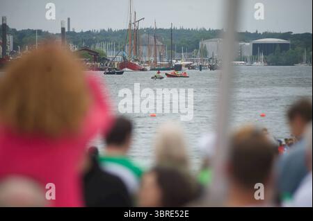 Flensburg, Schleswig-Holstein Flensburger Drachenbootrennen. Viele Menschen stehen dicht gedrängt am Hafen und schauen auf das Wasser. Im Hintergrund sind Segelboote, rote Sonnenschirme und Fahnen zu sehen. Auf dem Wasser fahren kleine Boote, am Ufer sind Industriegebäude und Bäume sichtbar. Aufnahme vom 12.07.2025, Flensburg, Hafen West, Hafenspitze *** Flensburg, Schleswig Holstein Flensburg Drachenbootrennen viele Menschen stehen überfüllt am Hafen und schauen auf das Wasser im Hintergrund sieht man Segelboote, rote Schirme und Fahnen kleine Boote segeln auf dem Wasser, Industriebauten und Tre Stockfoto