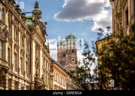 Ikonische Kathedrale unserer lieben Lieben Frau in München: Majestätische Doppelkuppeln, die sich über historischen Gebäuden unter Einem hellen blauen Himmel mit malerischen Wolken in der Nähe von Marie erheben Stockfoto