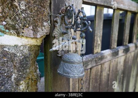 Rustikale Metallglocke an einem hölzernen Gartentor im Freien. Dorking, England Stockfoto