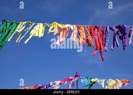 Regenbogenfarbene Lumpen oder Wimpel, an Linien angereiht, fliegen im Wind gegen einen blauen Himmel Stockfoto