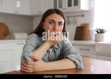 Verängstigte Frau, die an Paranoia leidet, am Tisch in der Küche Stockfoto
