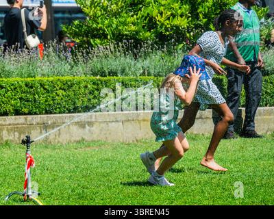 London, Großbritannien. Juli 2025. Eine weitere Mini-Hitzewelle führt zu sonnigem Wetter und Touristen reagieren, indem sie im Kühlwasser der Sprinkler für das Gras auf dem Parliament Square spielen. Guy Bell/Alamy Live News Stockfoto