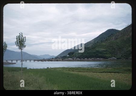 Ein malerischer Blick auf eine Brücke und ein traditionelles Fischerdorf entlang der Küste zwischen Masan und Chinhae (heute beide Teil von Changwon), Provinz Süd-Gyeongsang, Südkorea, aufgenommen im August 1956. Die Häuser mit Strohdach am Fuße eines üppigen Berges repräsentieren das ländliche Leben der Nachkriegszeit in Südkorea. Dieses Foto wurde von Chief Petty Officer Wilfred K.C. Park, einem koreanischen Amerikaner, der in der US Navy diente, aufgenommen, der das tägliche Leben und militärische Aktivitäten in Korea und Japan während der 1950er Jahre dokumentierte Stockfoto