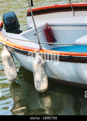 Ein Fischerboot mit einem kleinen Motor liegt in ruhigen Gewässern vor Anker. Zwei Kotflügel hängen an der Seite und erzeugen sanfte Wellen. Stockfoto